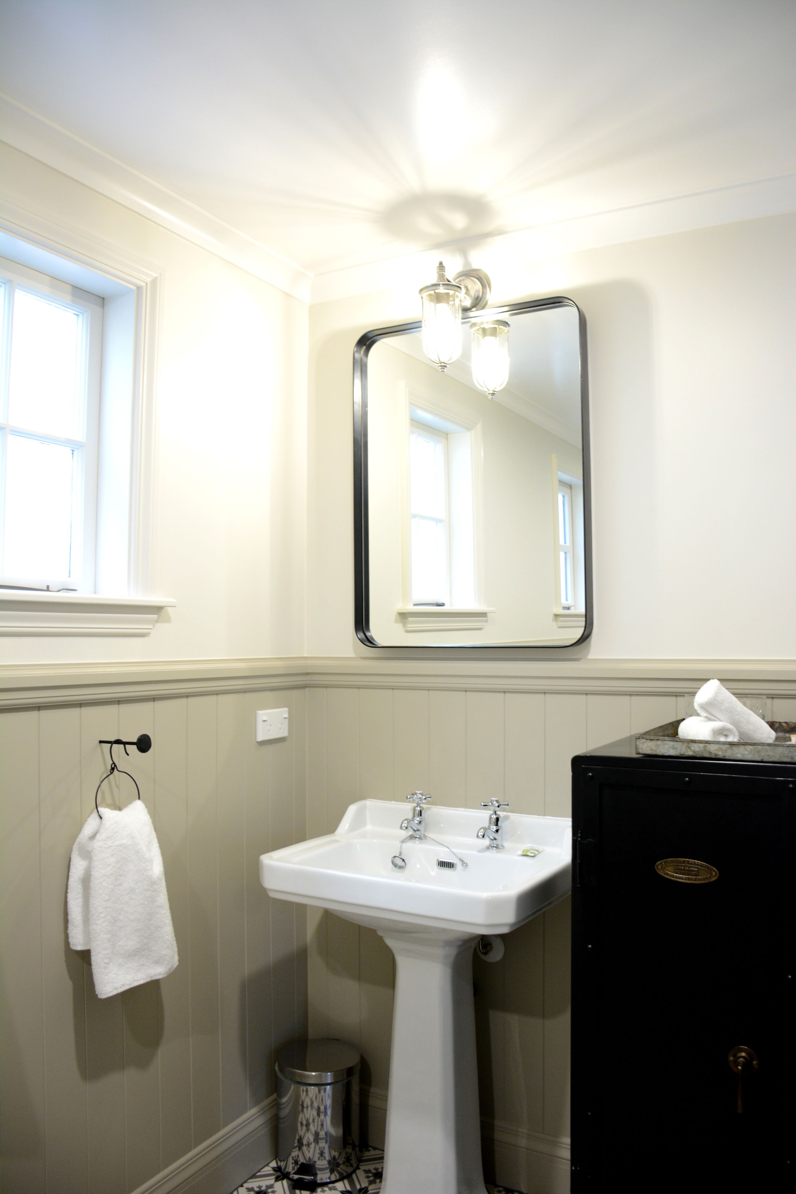 A bathroom with a pedestal sink, a mirror, a towel rack, and a trash can.