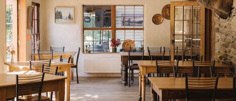 Un coin repas avec des tables et des chaises en bois, une grande fenêtre offrant une belle vue et une tête de cerf fixée au mur.
