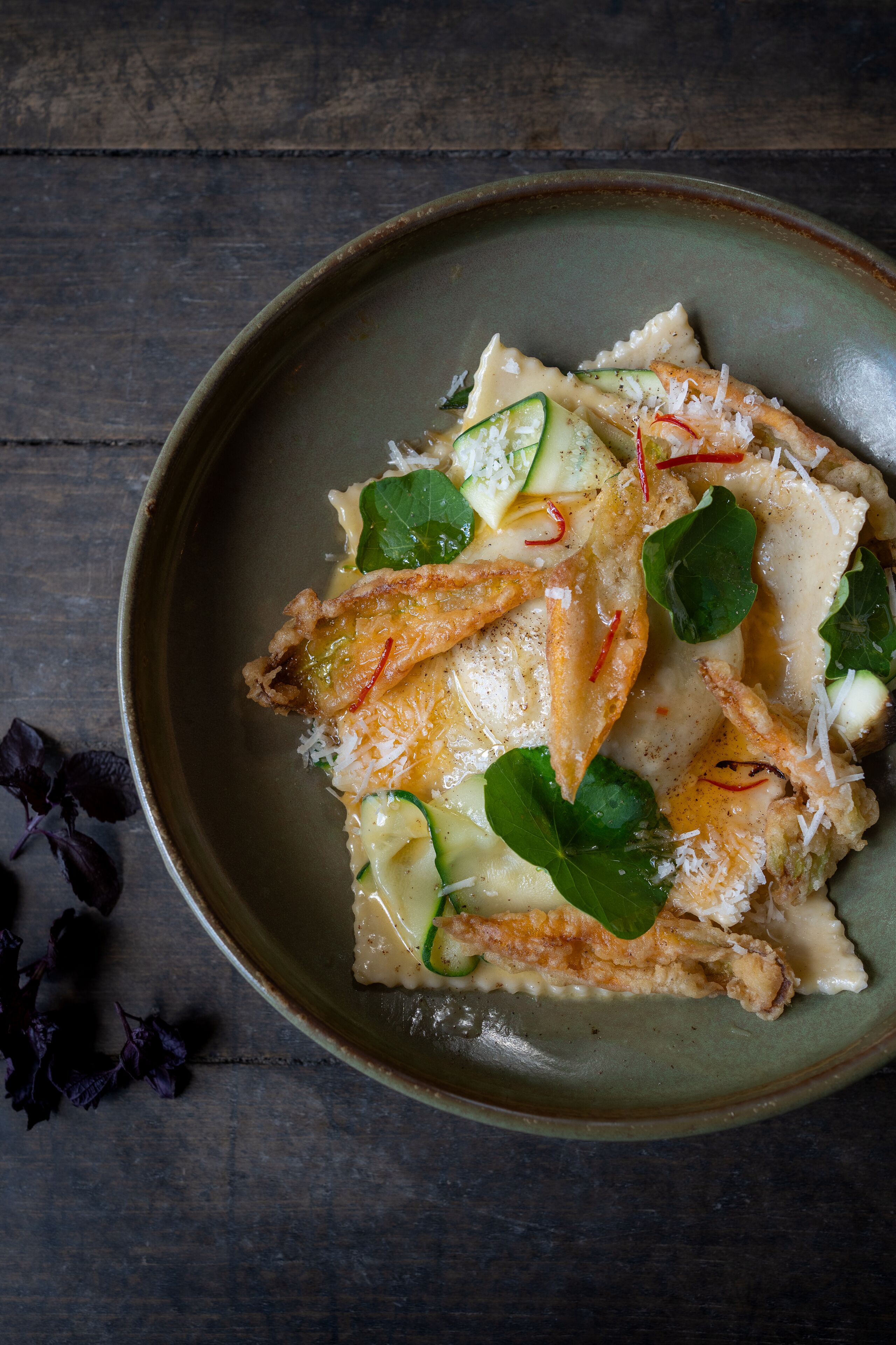 A plate of food with pasta, zucchini, and greens on a rustic wooden table.