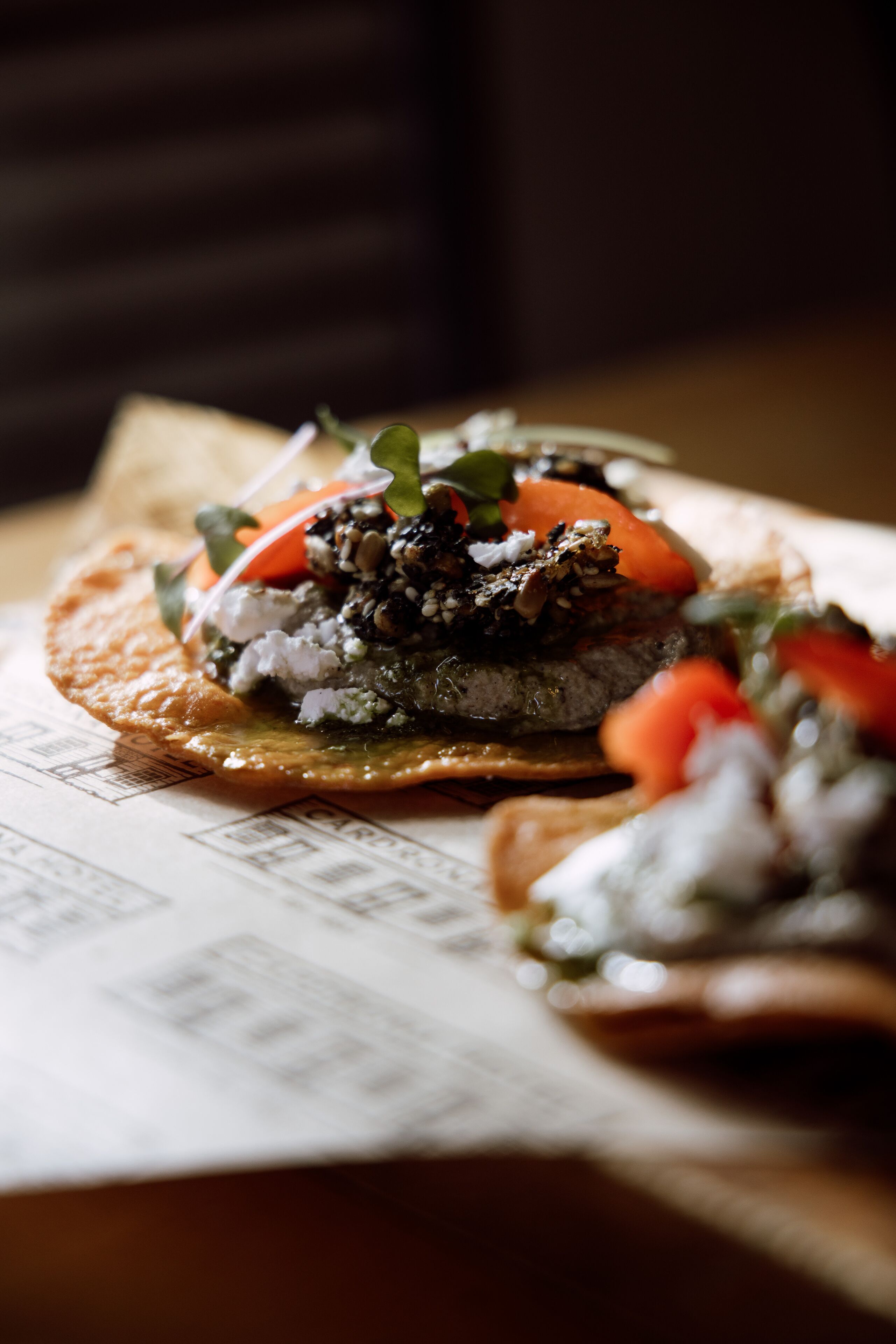 A close-up of a dish with a variety of toppings, including vegetables and possibly some grains or seeds, on a flatbread or similar base.