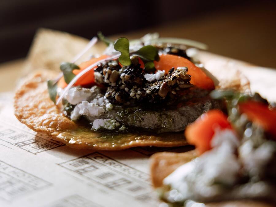 A close-up of a dish with a variety of toppings, including vegetables and possibly some grains or seeds, on a flatbread or similar base.