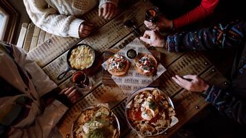 Uma mesa de madeira com comida e bebidas, rodeada por pessoas.