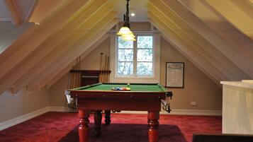 A pool table in a room with sloped ceilings and a large window.