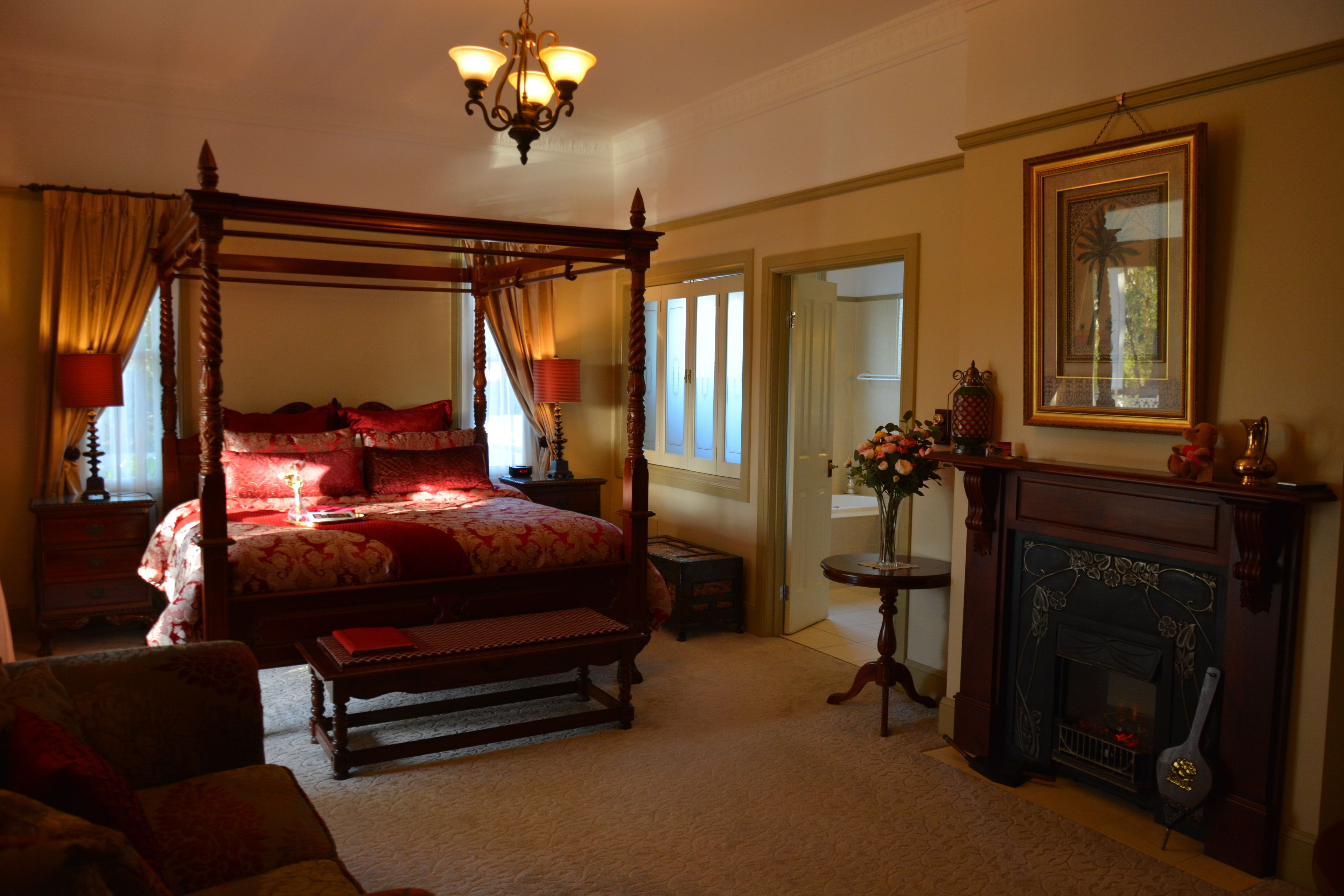 A four-poster bed with red bedding, a fireplace, and a chandelier.