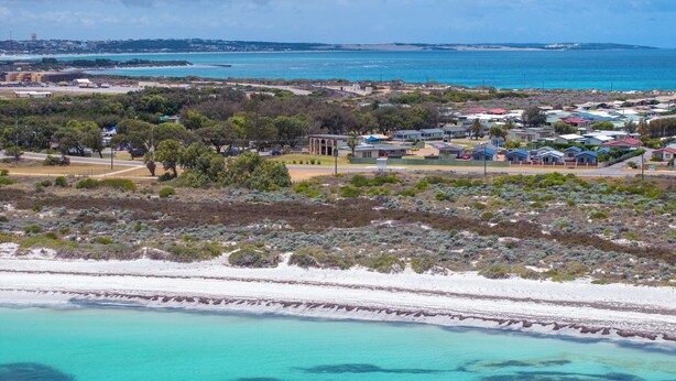 Une zone côtière comprenant une plage, des immeubles résidentiels et une vue lointaine sur une ville.