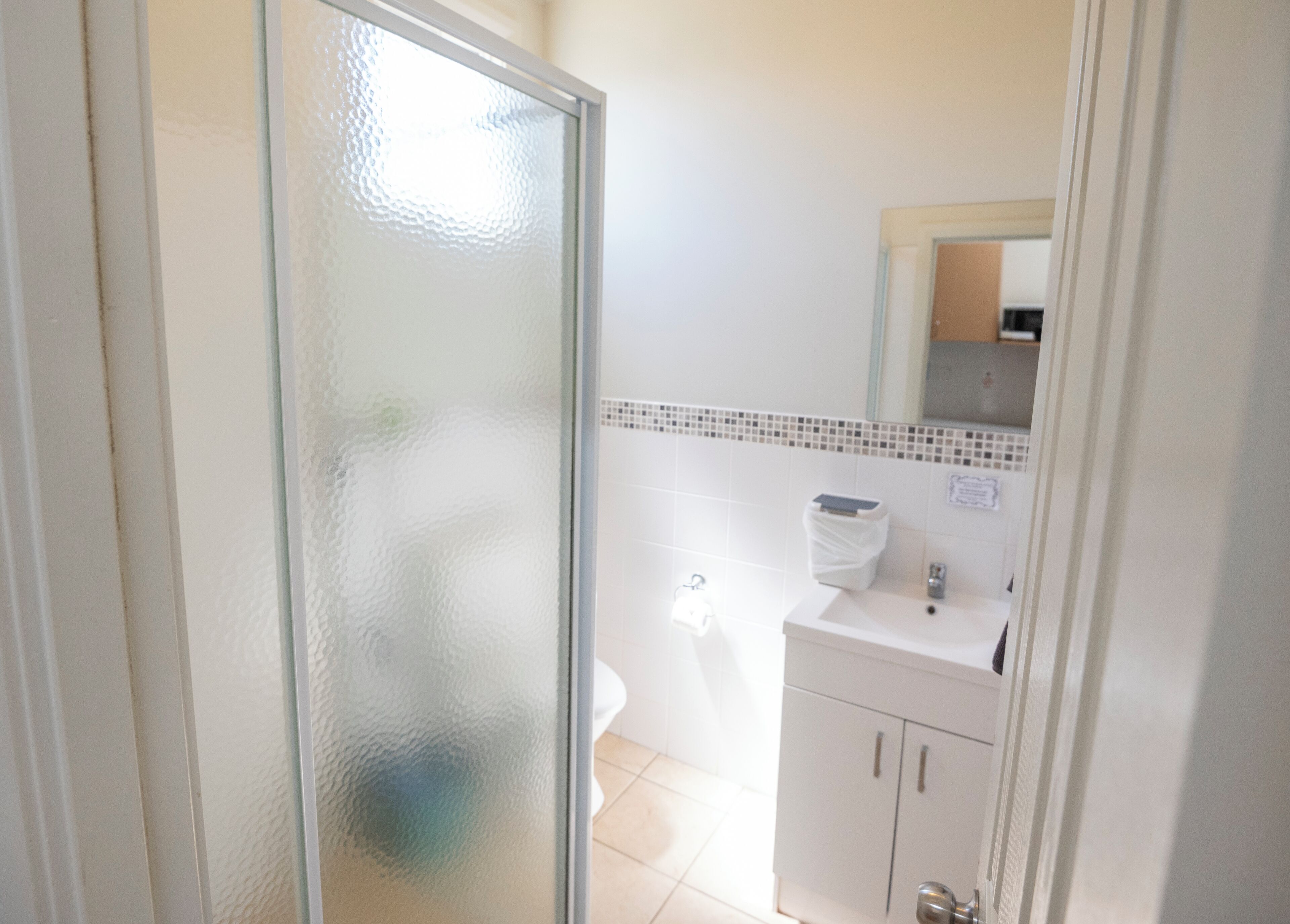 Ein Badezimmer mit Duschabtrennung aus Glas, einem weißen Waschbecken, einem Spiegel und einer gefliesten Rückwand.