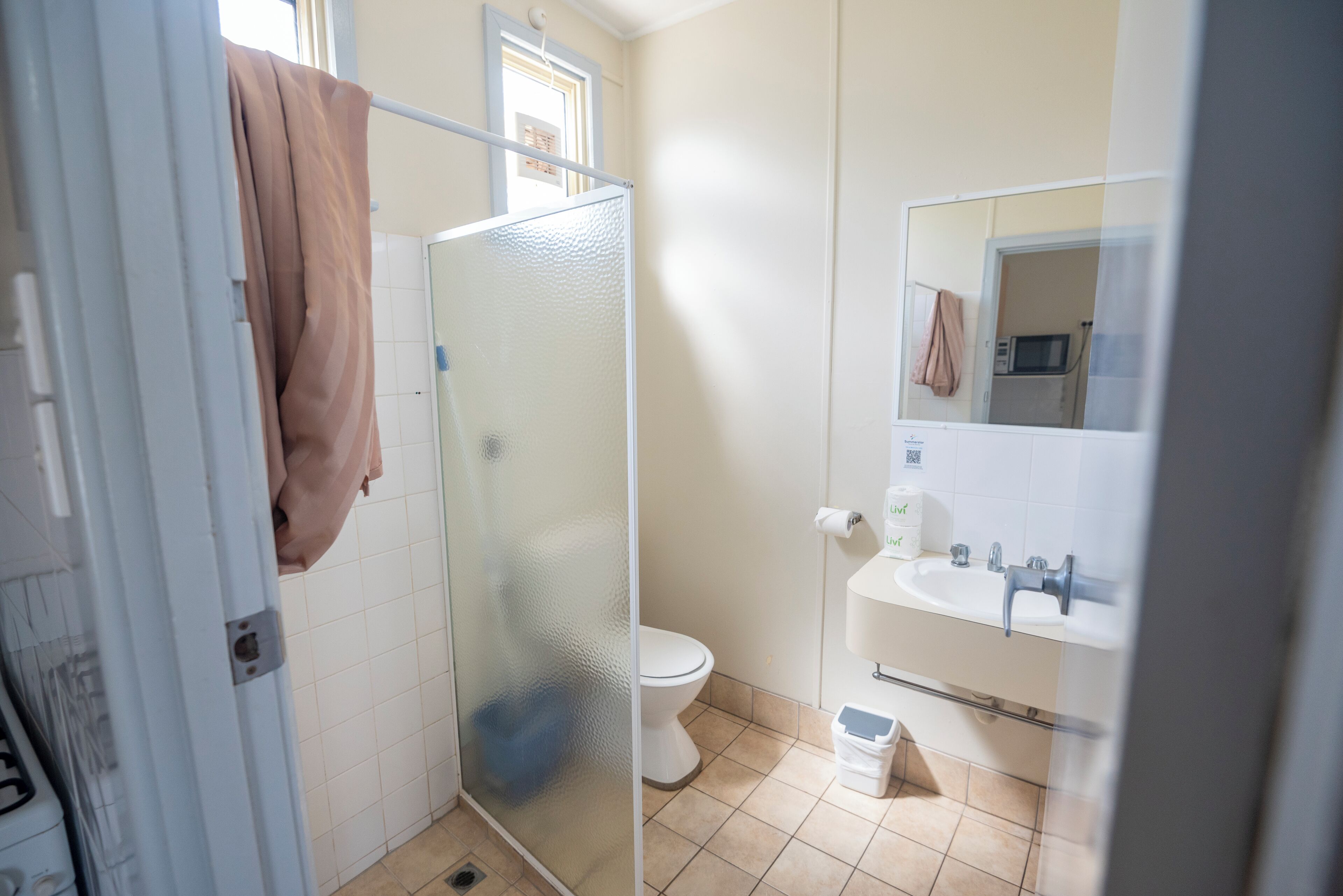 Een badkamer met een douchecabine van glas, toilet, wastafel en spiegel.