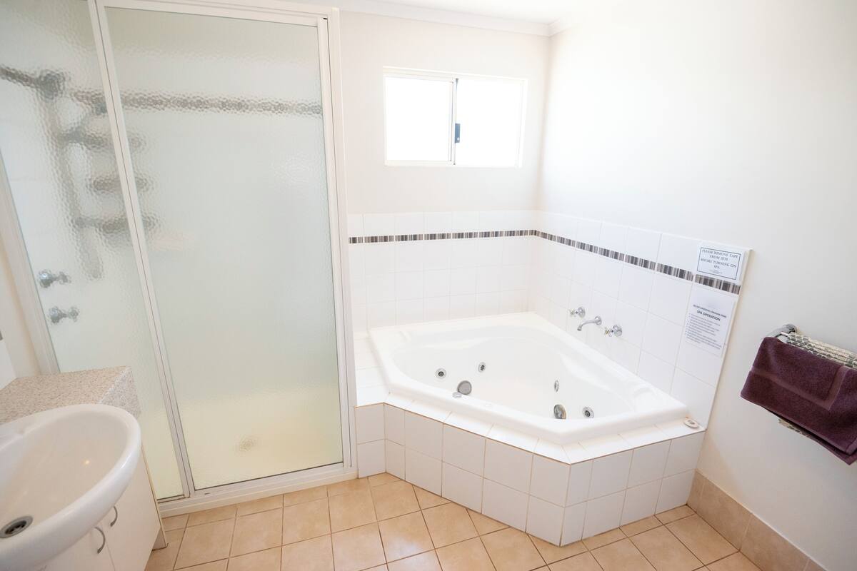 Een badkamer met een douchecabine van glas, een wit ligbad en een wastafel.