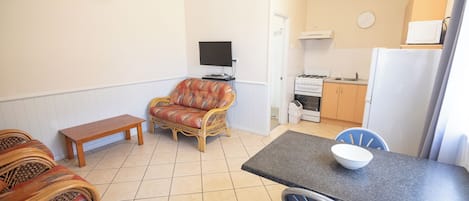 Un espacio habitable compacto con sofá, una mesa de comedor con sillas, un televisor, una cocina con estufa y refrigerador, además de un banco.
