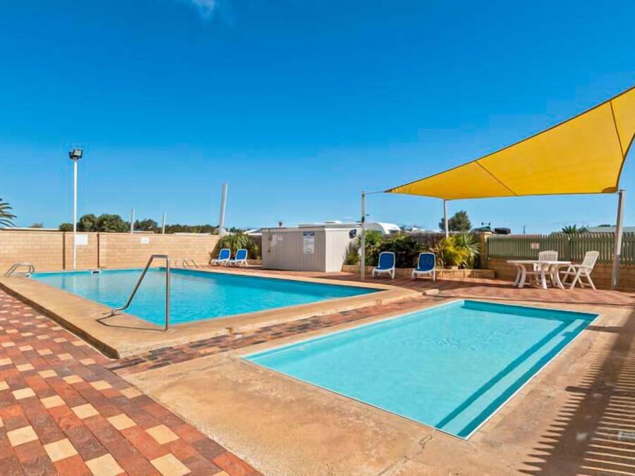 Zona de piscina con dos piscinas, sillas de descanso y sombra.