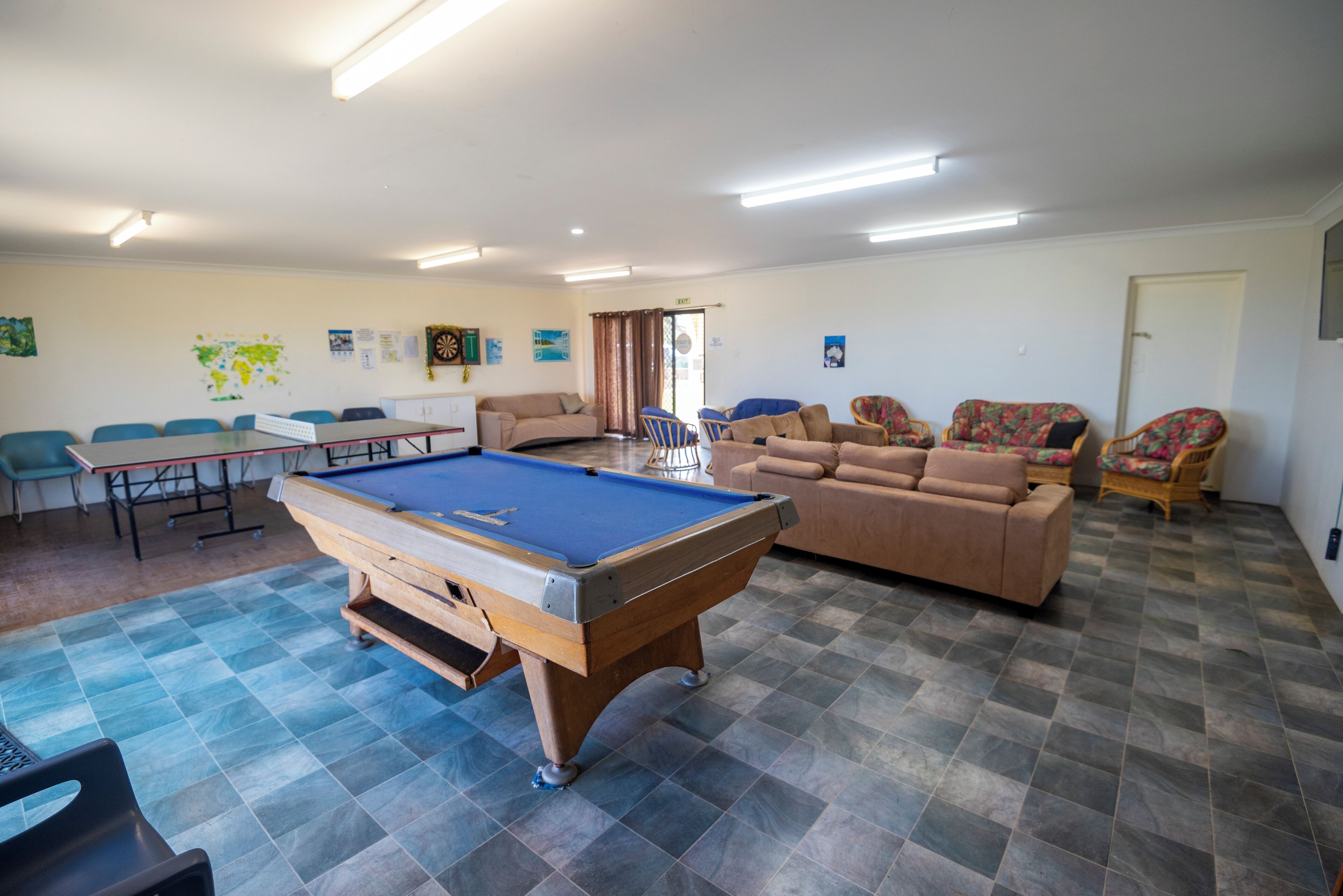 A pool table in a room with a sofa, chairs, and a map on the wall.