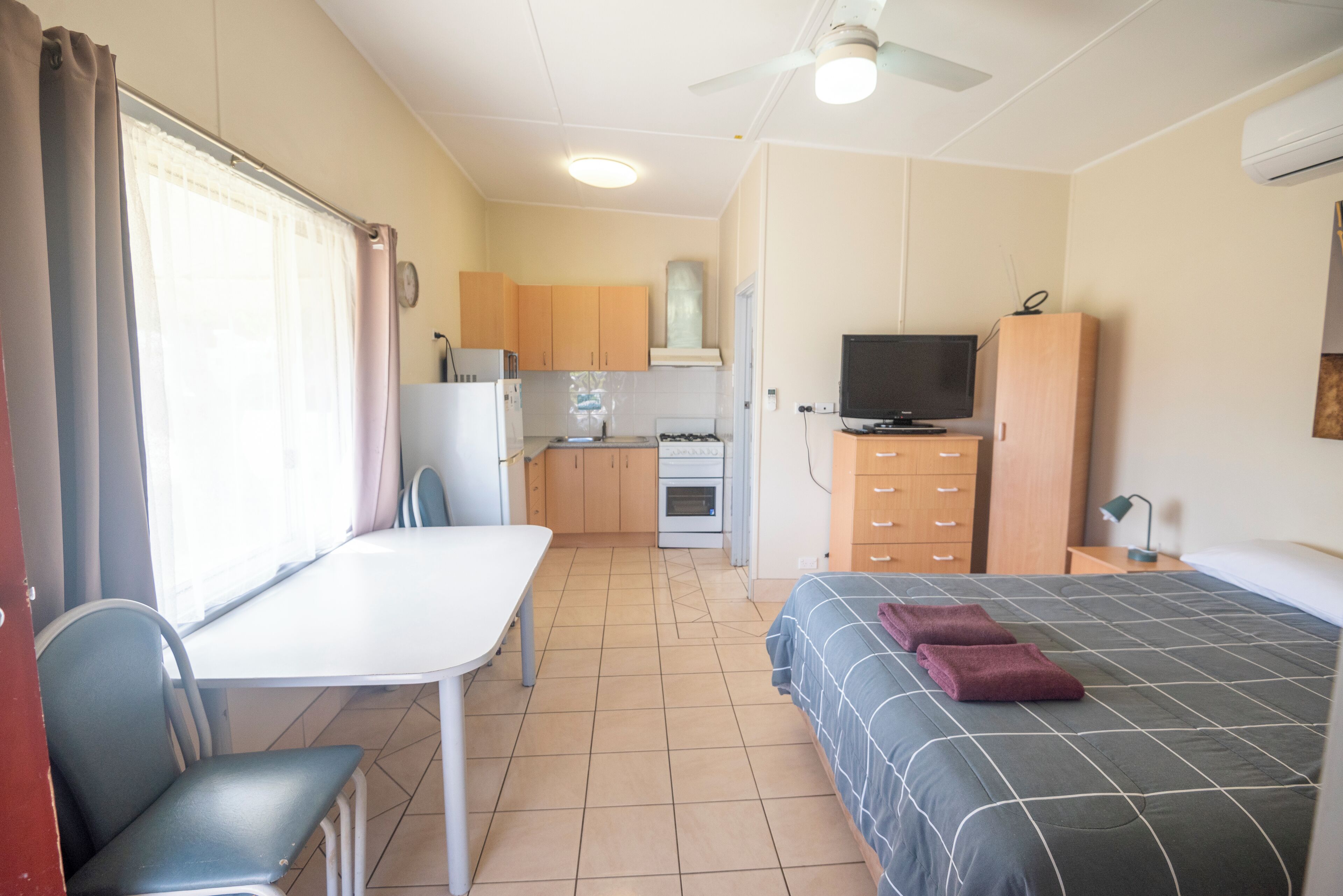 Una habitación compacta con cama, una kitchenette pequeña, una mesa de comedor y televisión.