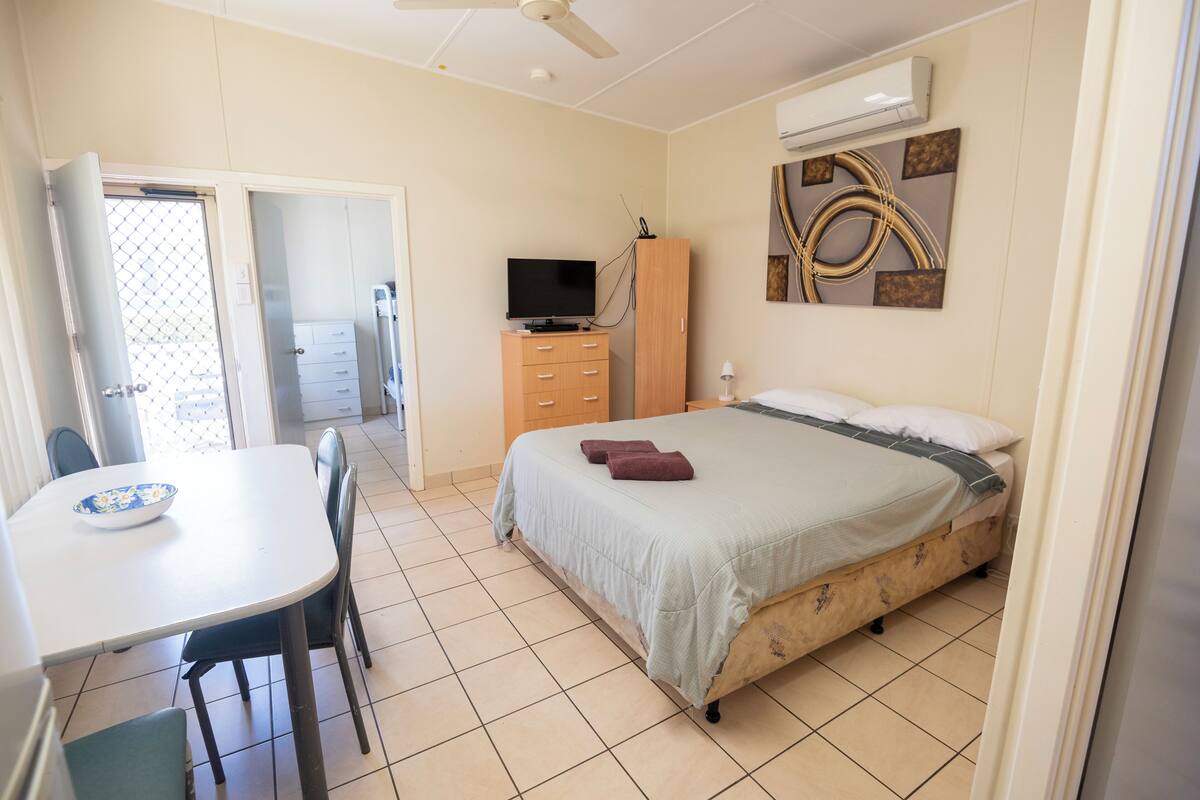 Een slaapkamer met een bed, een televisie, een kledingkast, een bureau met stoel en een eettafel.
