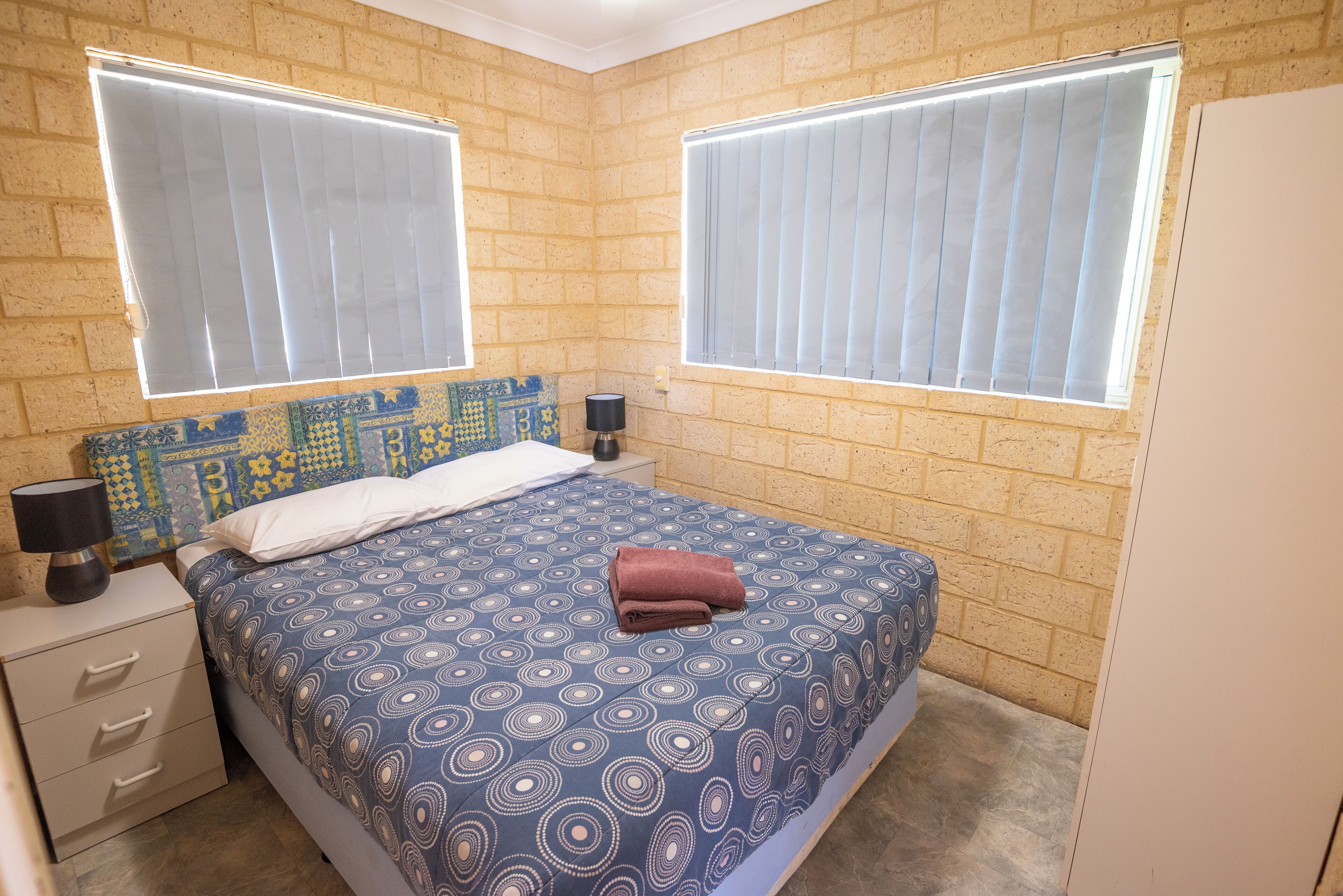 A bedroom with a patterned bedspread, two bedside lamps, a nightstand, and a brick-patterned headboard.