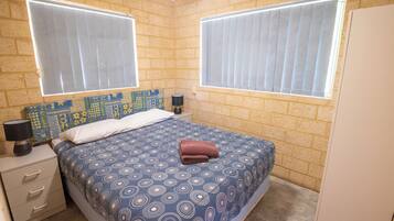 A bedroom with a patterned bedspread, two bedside lamps, a nightstand, and a brick-patterned headboard.