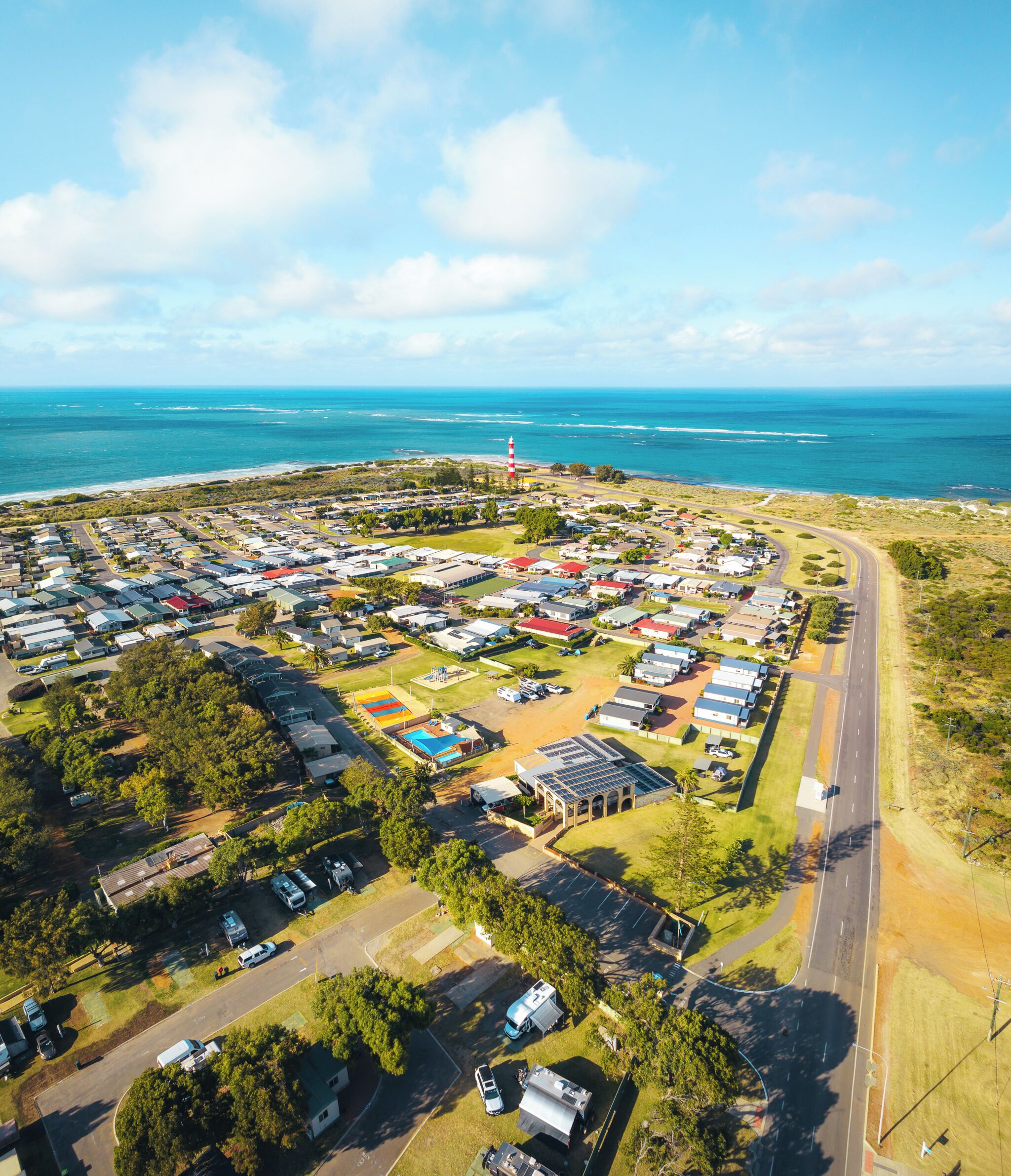 An aerial view of a coastal residential area with houses, a road, and a lighthouse.