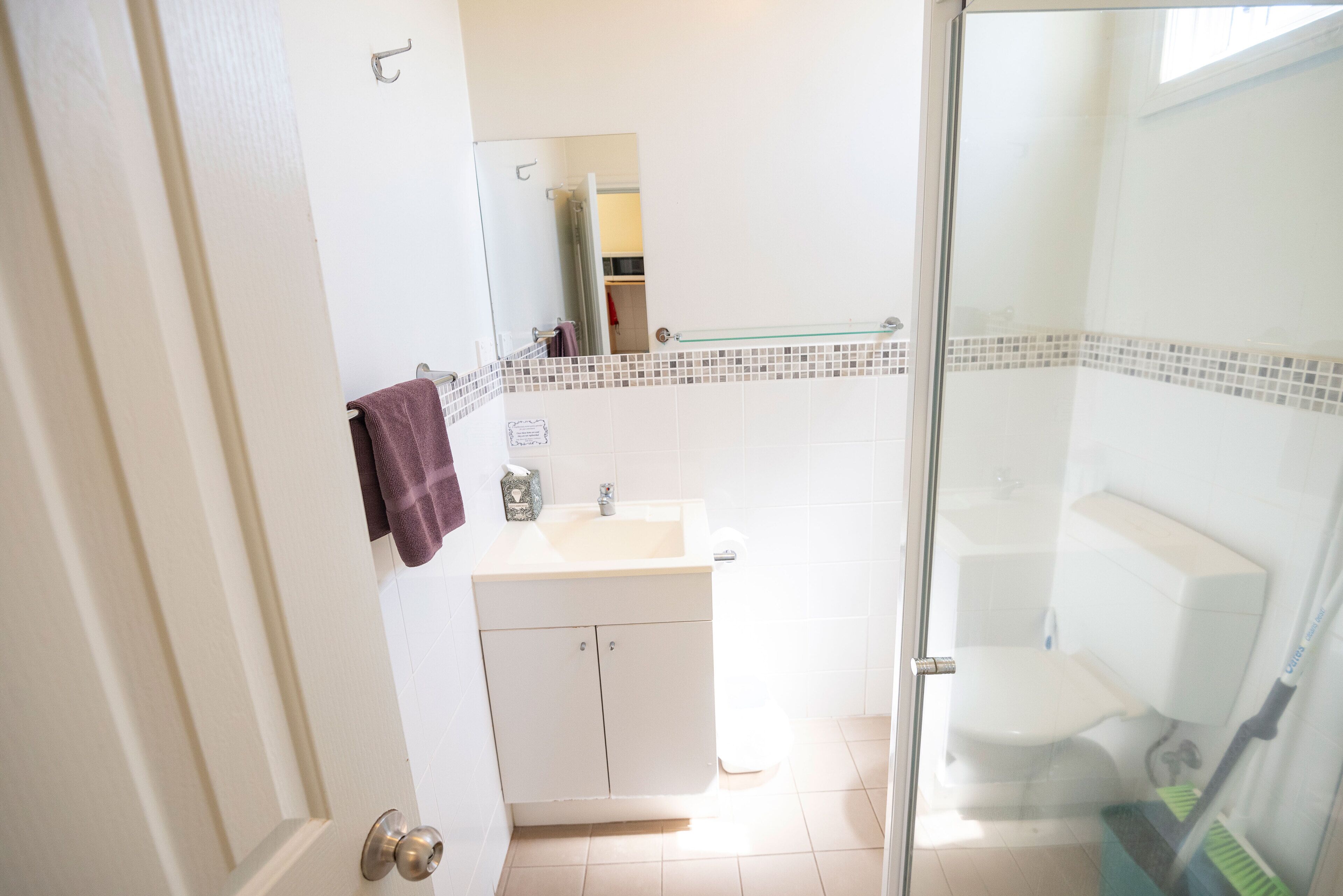 A bathroom with a glass shower door, a white sink, and a tiled backsplash.