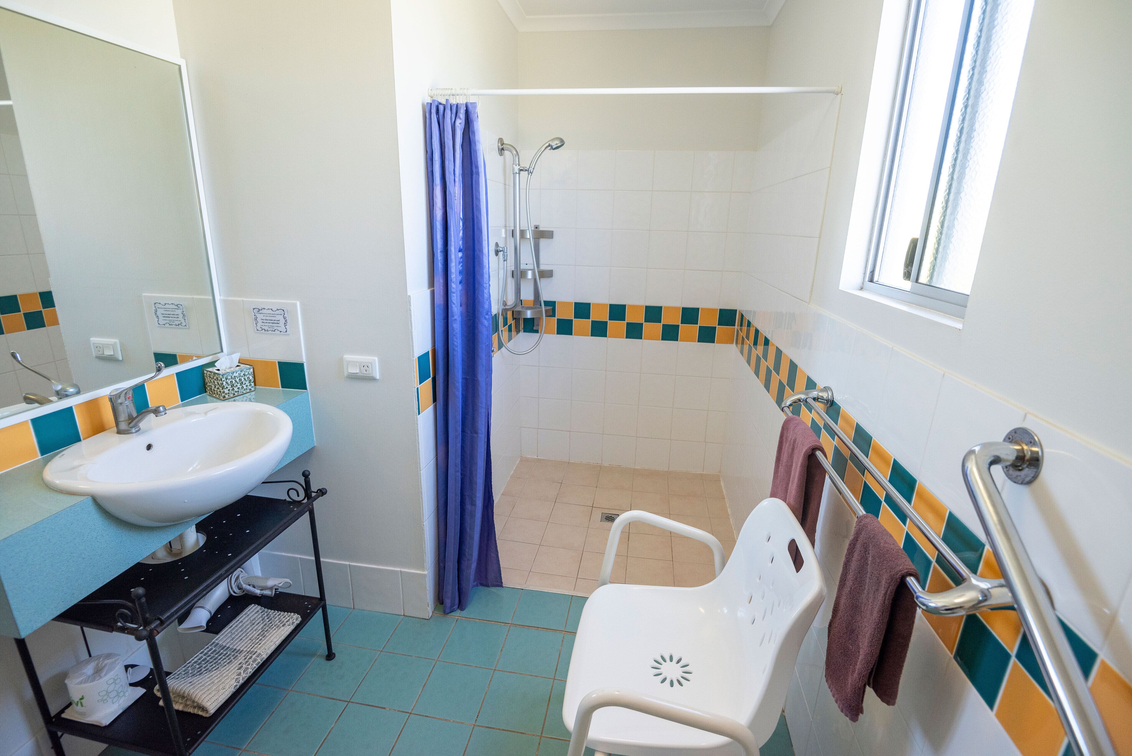 A bathroom with a sink, mirror, shower, and a window.
