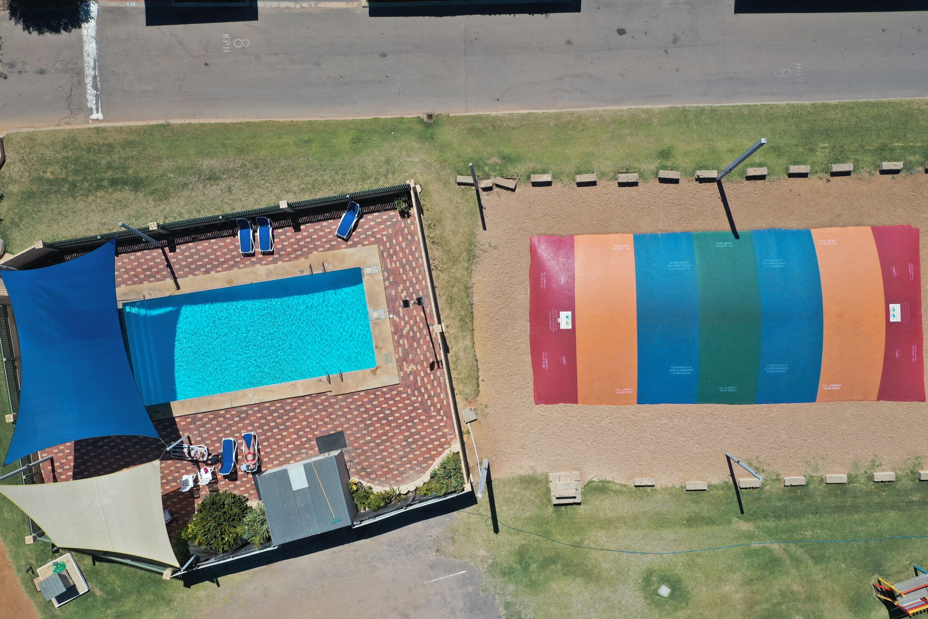 Vista aérea de un hotel con piscina, un patio cubierto y una zona de playa arenosa con colchonetas de colores.