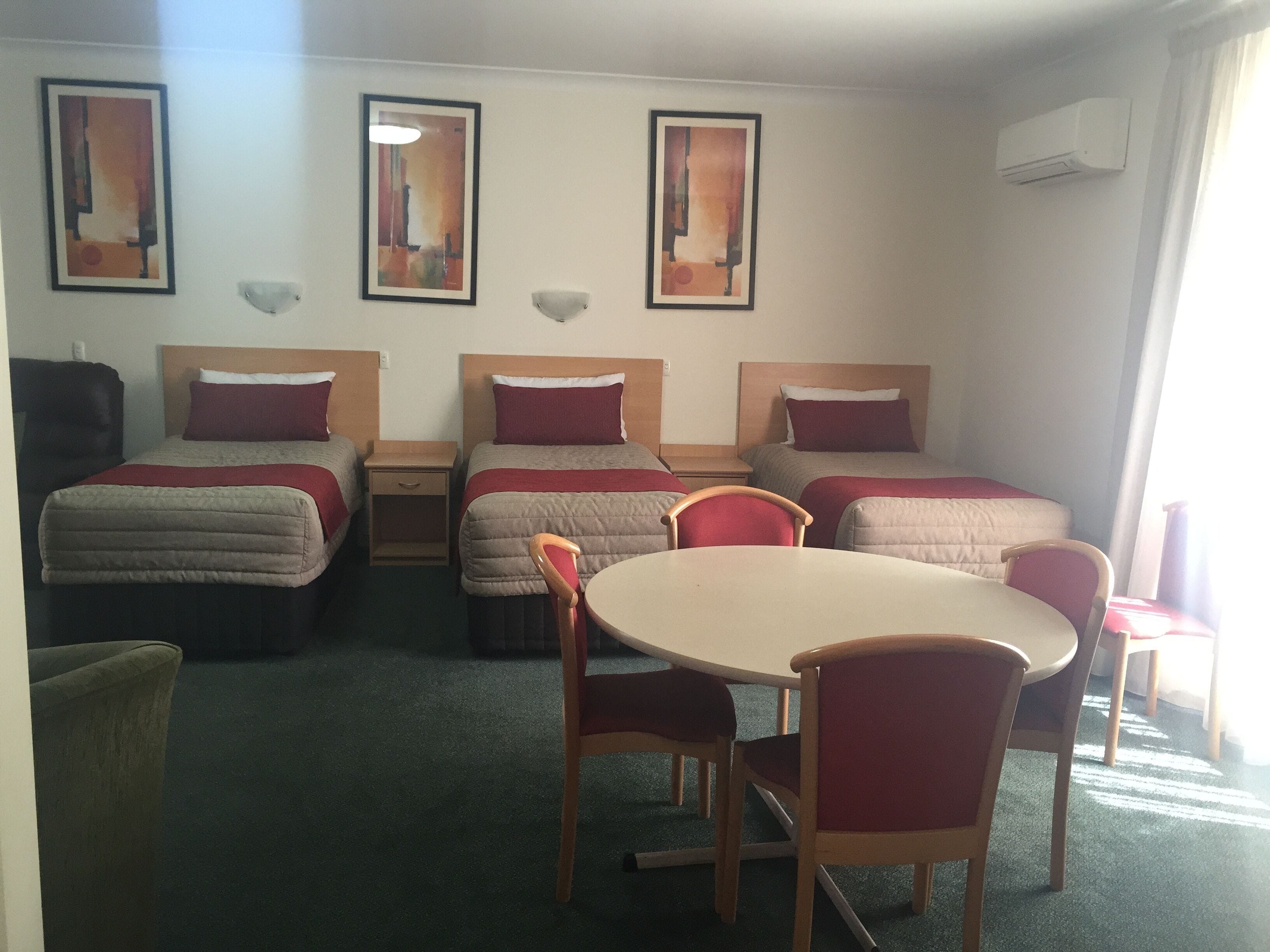 A hotel room with two single beds, a round table, and two chairs. There are three framed artworks on the wall.
