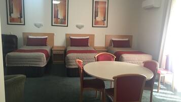 A hotel room with two single beds, a round table, and two chairs. There are three framed artworks on the wall.