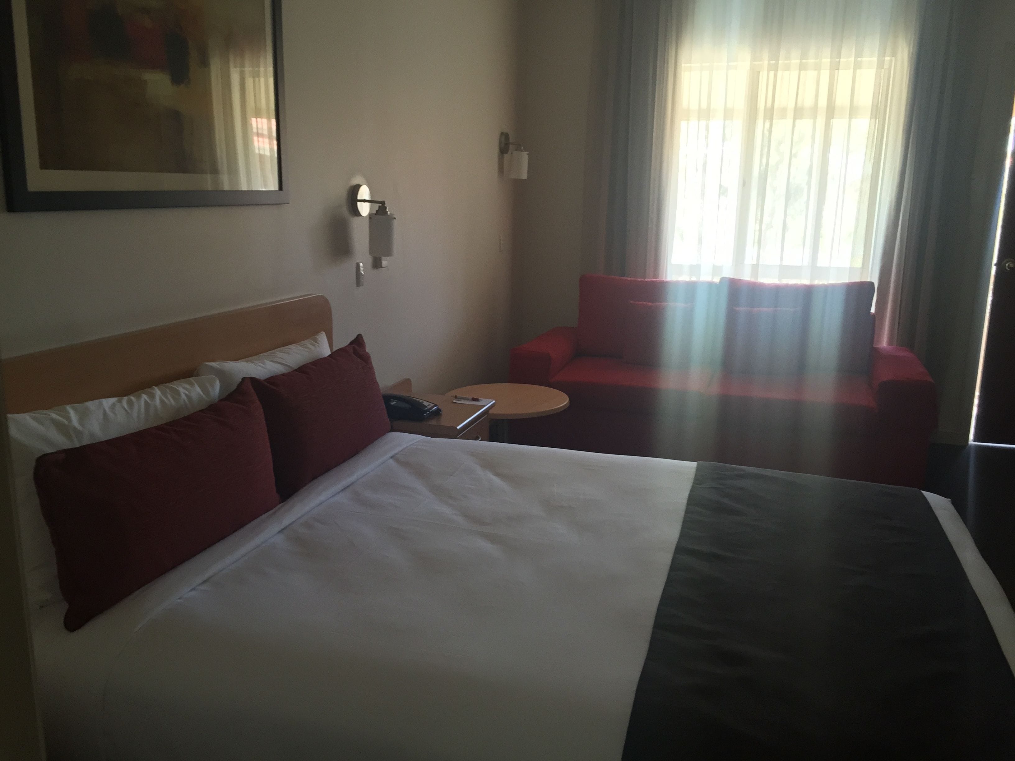 A hotel room with a large bed, a red sofa, a small round table, and a painting on the wall.