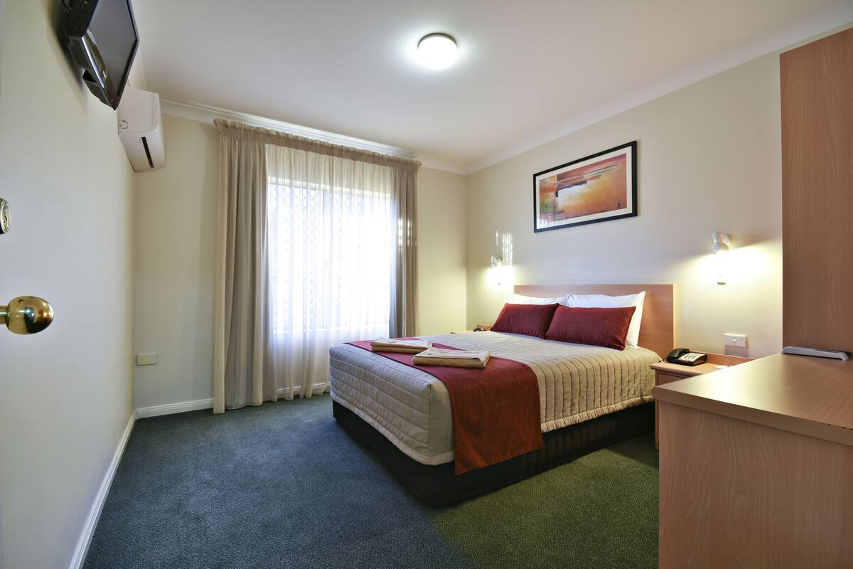A hotel room with a bed, a desk, a TV, and a window with curtains.