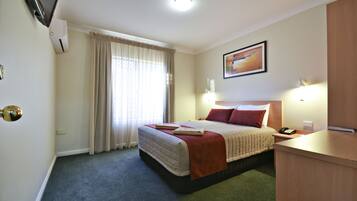 Een hotelkamer met een bed, een bureau, een televisie en een raam met gordijnen.