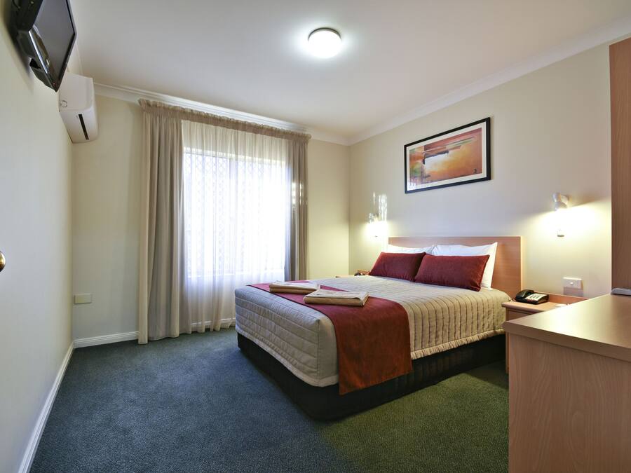 Een hotelkamer met een bed, een bureau, een televisie en een raam met gordijnen.