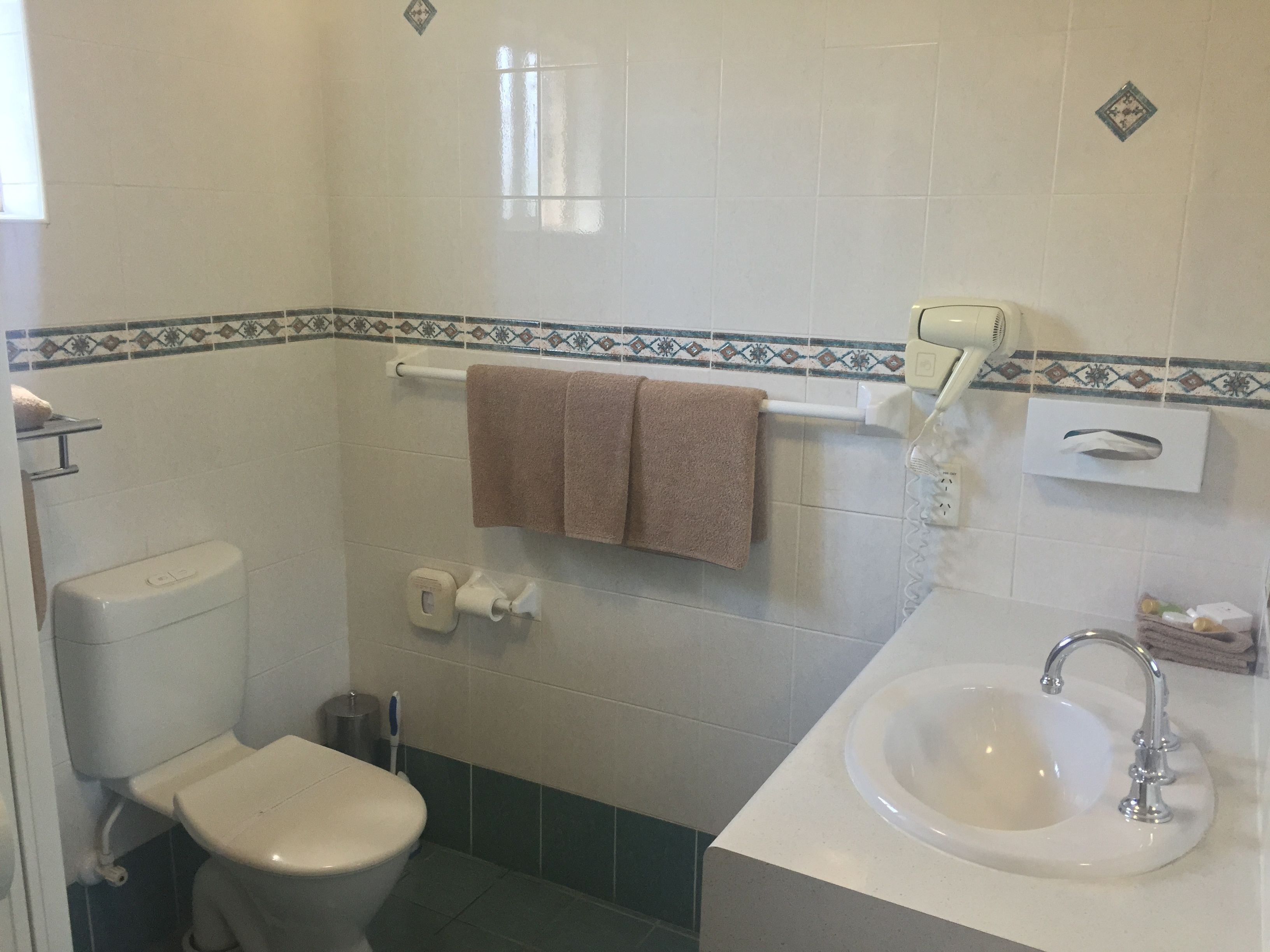 A bathroom with a toilet, sink, towel rack, and a hand dryer.