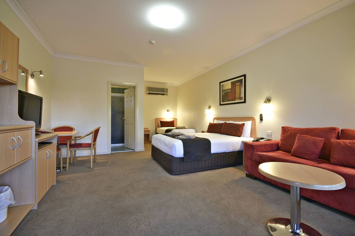 A hotel room with a bed, a desk, a chair, a couch, and a TV.