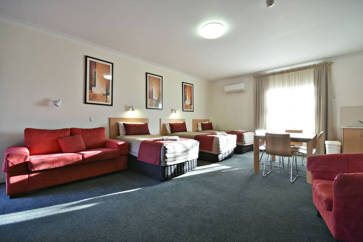 A hotel room with two red sofas, a dining table with chairs, and three beds.