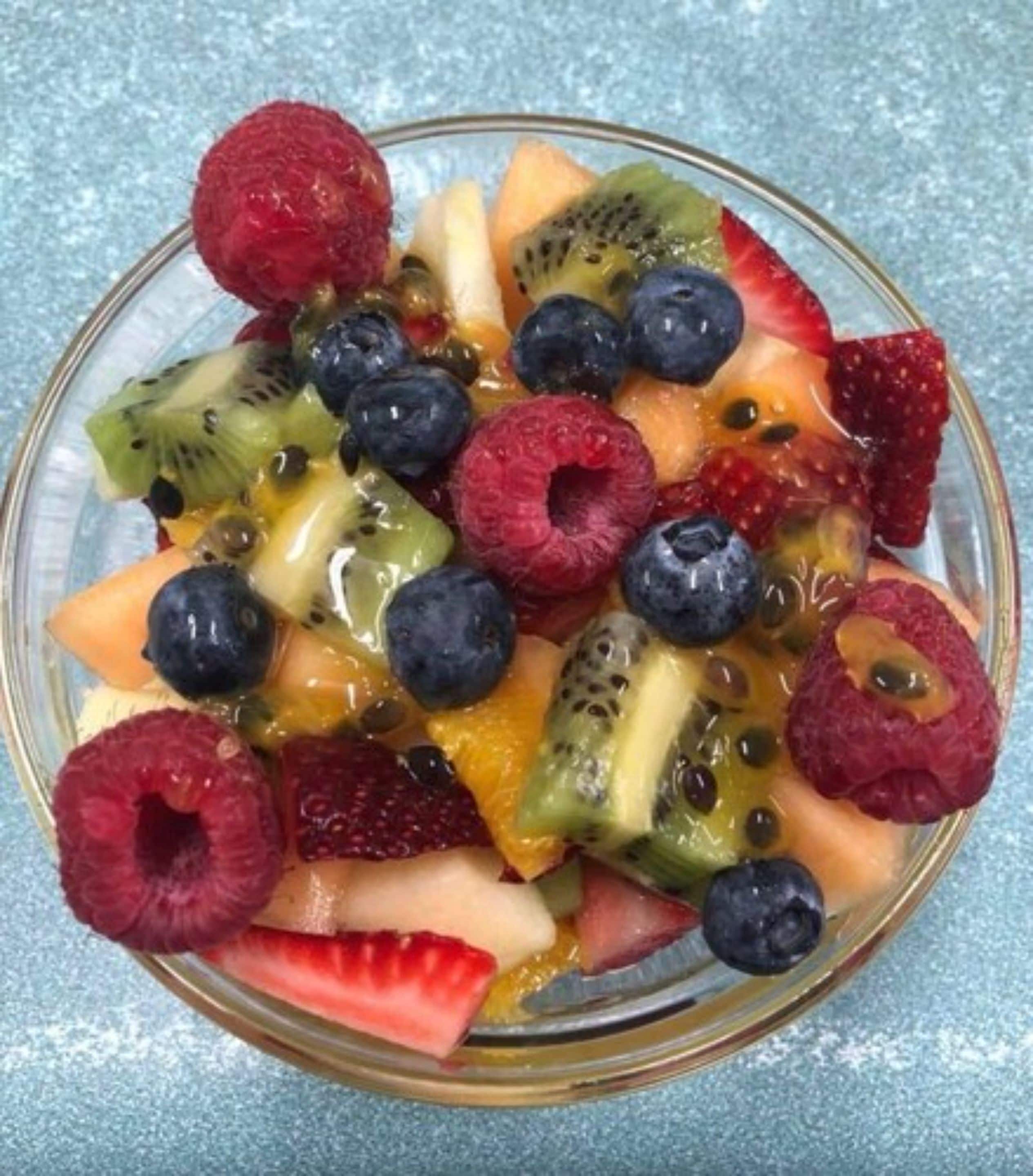 A bowl of mixed fruit including strawberries, blueberries, raspberries, kiwi, and melon.