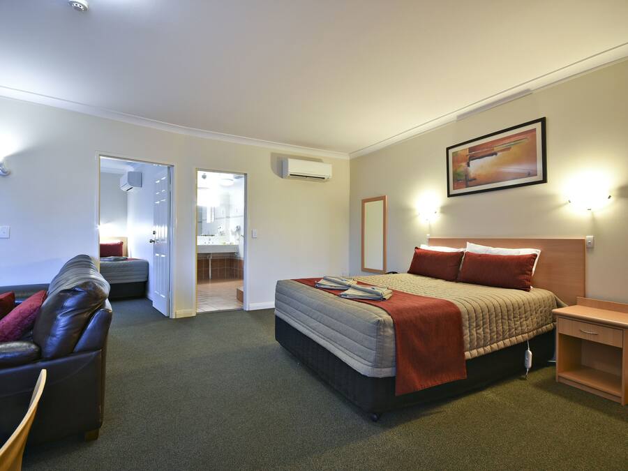 Een hotelkamer met een bed, een slaapbank, een nachtkastje en een badkamer zichtbaar door een geopende deur.