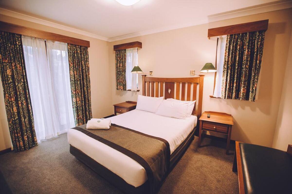Een hotelkamer met een groot bed, twee nachtkastjes, een houten hoofdeinde en gordijnen.