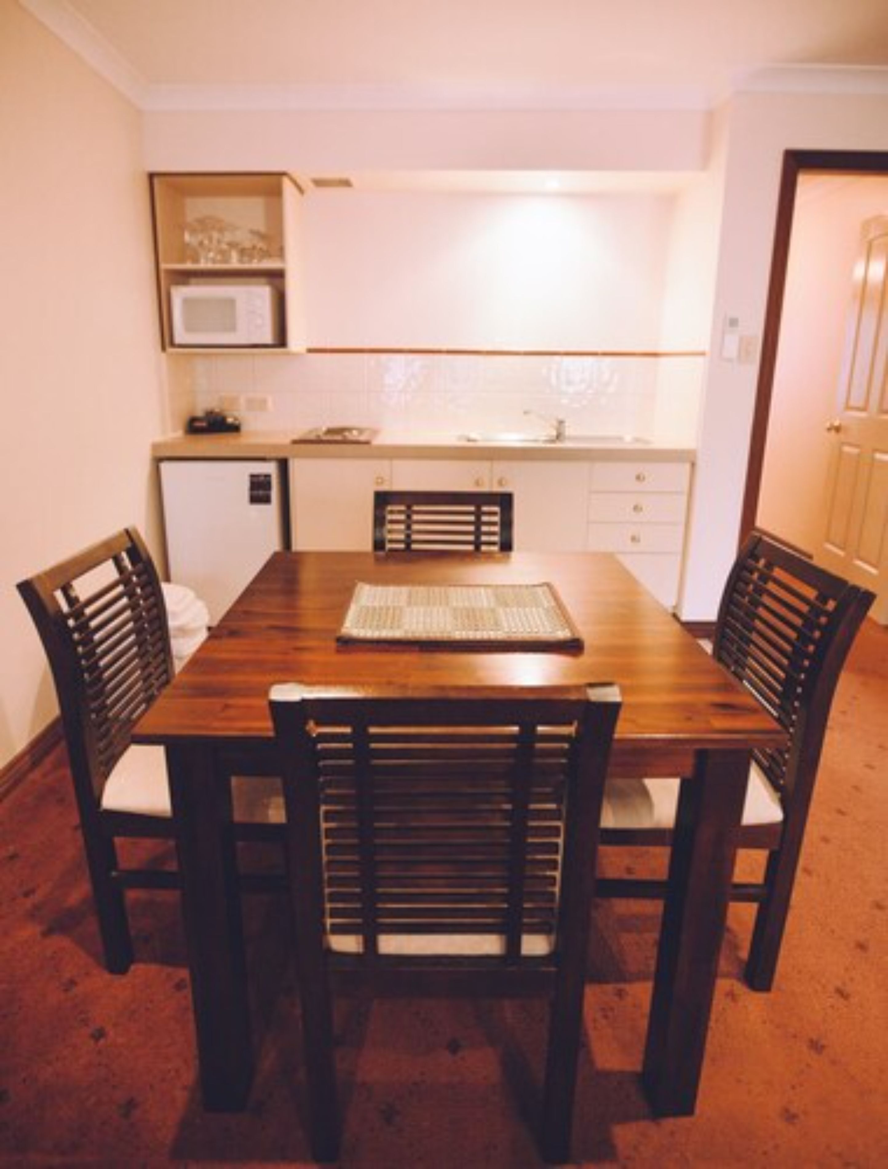 A compact kitchen with a dining table and chairs, a microwave, and a small refrigerator.