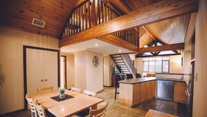 Una cocina amplia con vigas de madera, un comedor con mesa y sillas, y una escalera que conduce a un nivel superior.