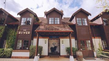 Welcome to The River, a charming building with a central entrance and two wings, featuring a welcoming porch area and potted plants.