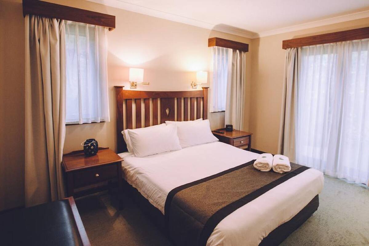 Een hotelkamer met een groot bed, twee nachtkastjes en een raam met gordijnen.