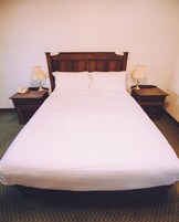 A standard hotel room with a single bed, two bedside tables, and a nightstand with a lamp.