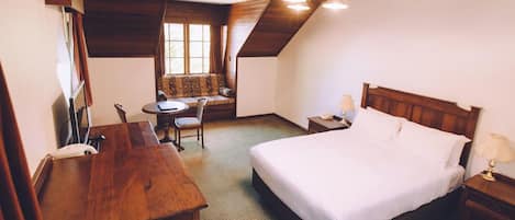 Habitación de hotel con una cama grande, un escritorio, una silla, una mesita y una ventana con vistas.