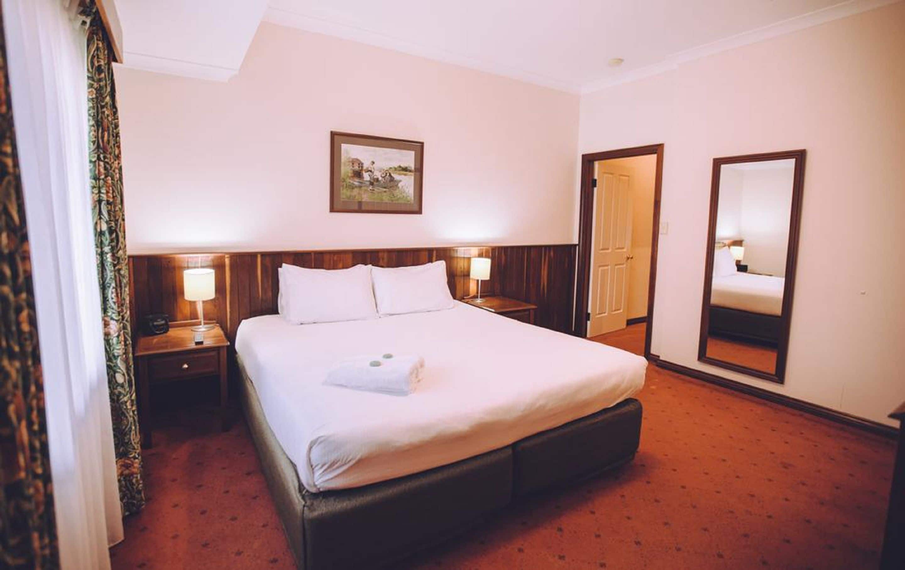 A hotel room with a large bed, two bedside lamps, a framed picture on the wall, and a mirror on the wall.