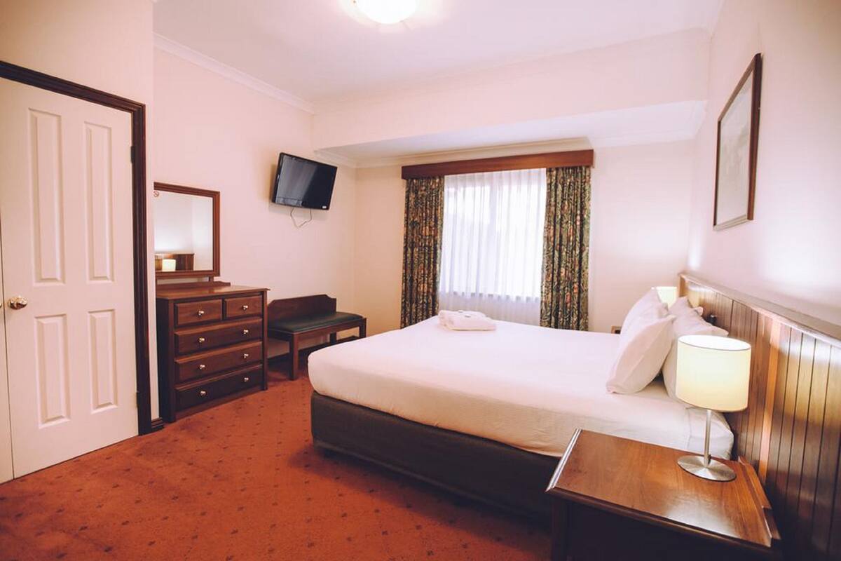 Een hotelkamer met een bed, een bureau, een dressoir, een televisie en een raam met gordijnen.