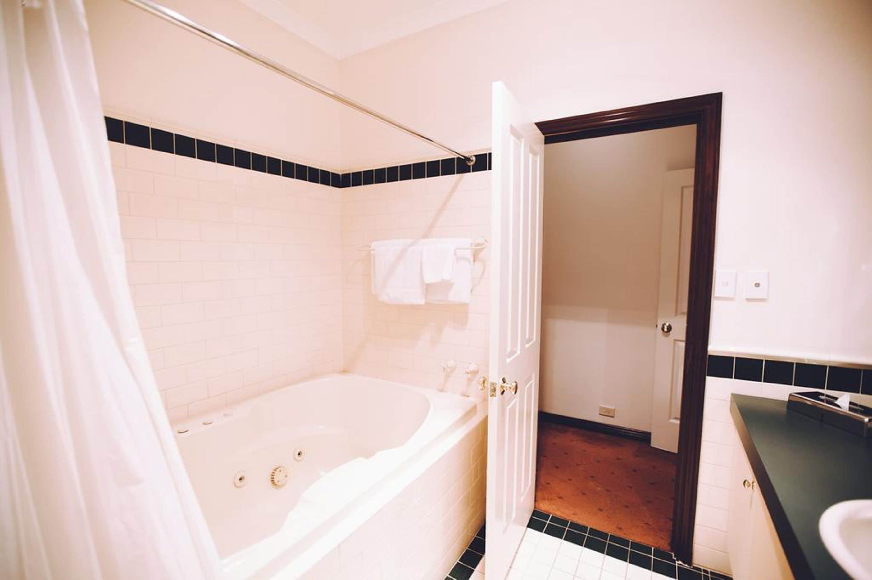 Une salle de bain avec une baignoire blanche, un rideau de douche, un porte-serviettes et une porte donnant sur une autre pièce.