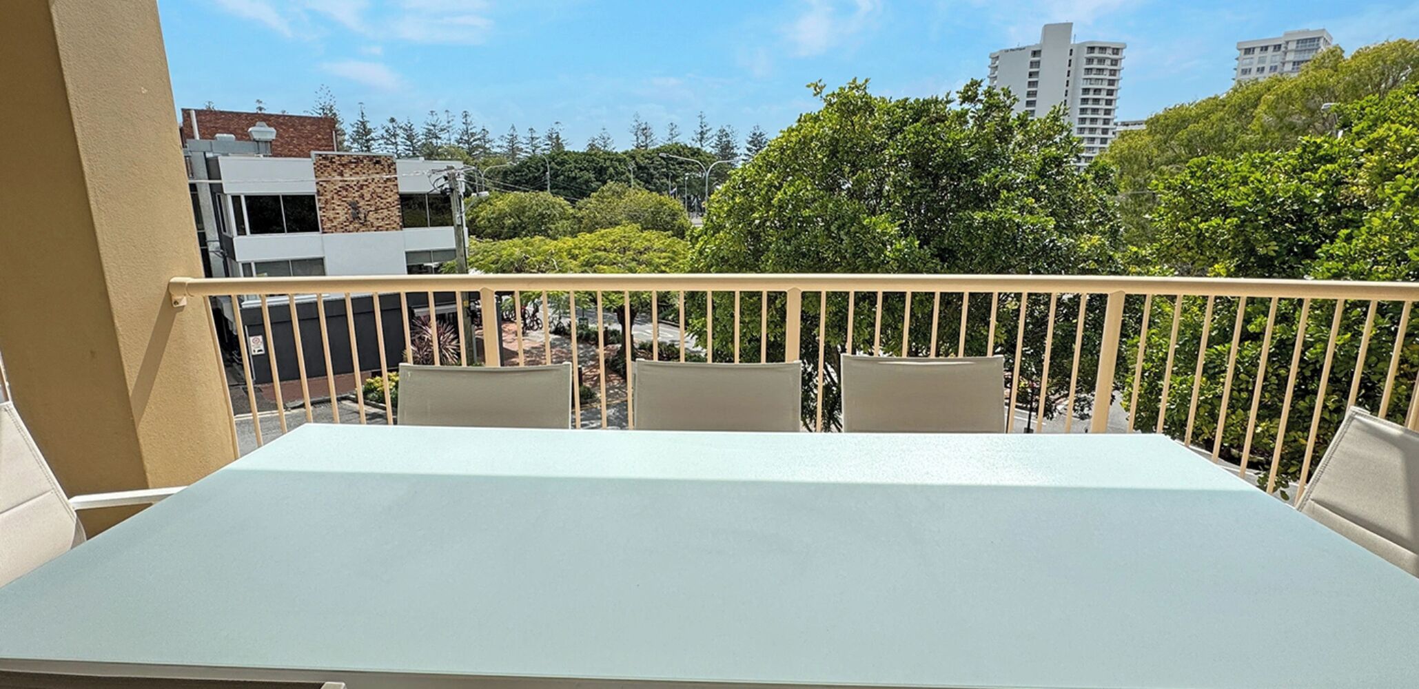 A balcony with a table and chairs, overlooking a cityscape with buildings and trees.