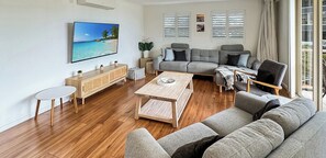 A modern living room with a sofa, a coffee table, a side table, and a television mounted on the wall. - The Village Holiday Apartments at Burleigh (Burleigh Heads)