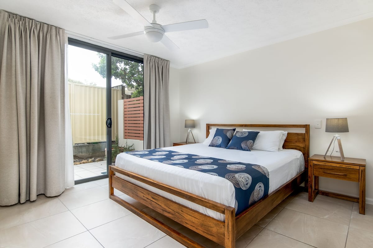 A bedroom with a wooden bed, two bedside tables, a ceiling fan, and a sliding glass door leading to an outdoor area.