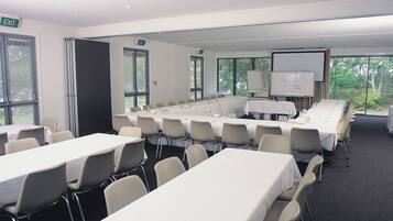 A conference room with multiple tables and chairs, a whiteboard, and a projector screen.
