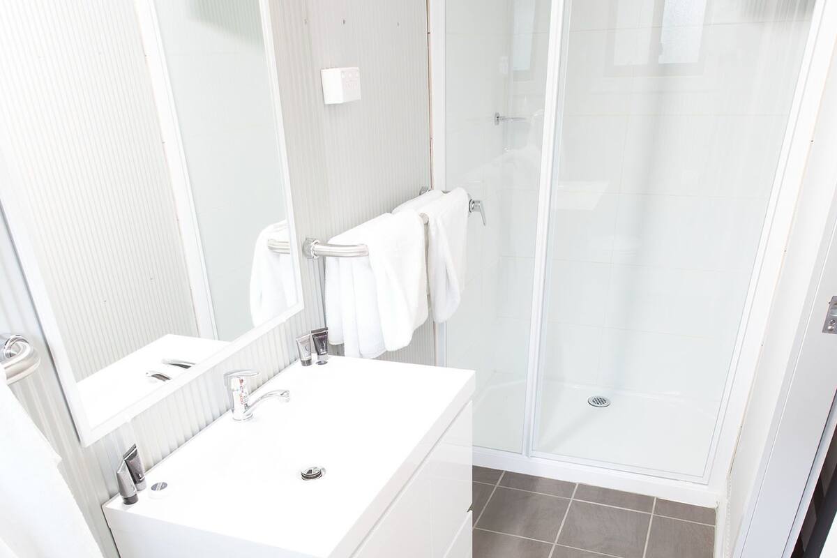 Une salle de bain moderne avec un lavabo blanc, un miroir et une cabine de douche en verre.