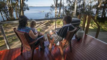 A family on a wooden deck overlooking a lake with a grill and propane tank.